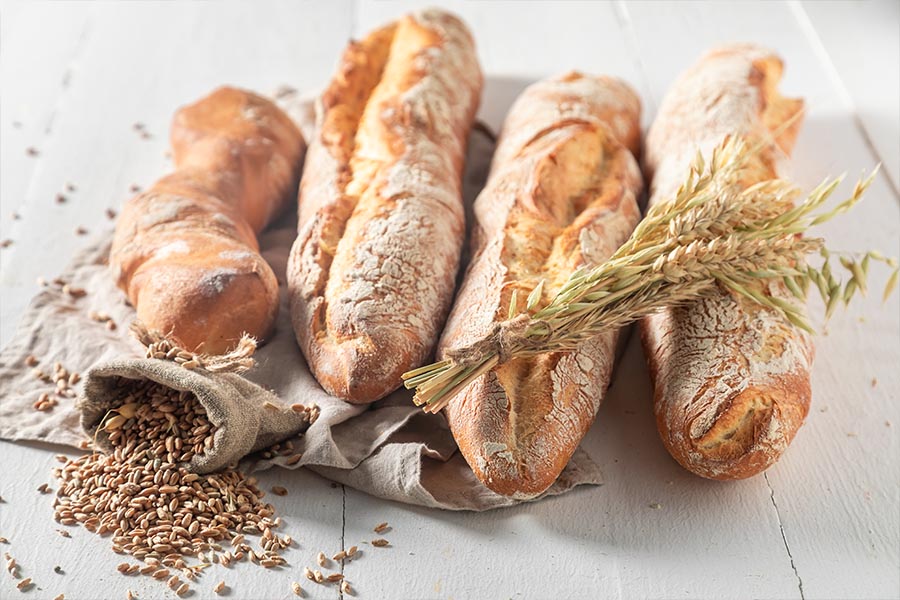Mehrere knusprige Baguettes mit Getreideähren und ausgeschüttetem Korn.