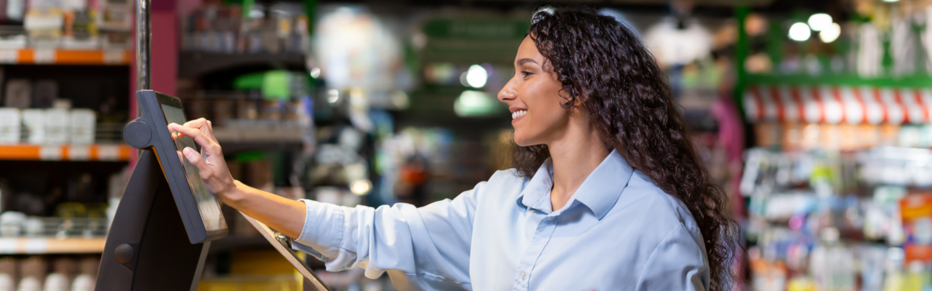 Kundin im Supermarkt wiegt Brokkoli an einer Selbstbedienungswaage mit Einkaufskorb.