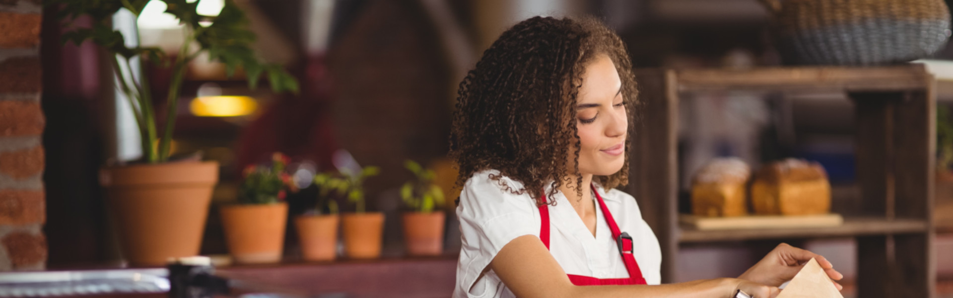 Mitarbeiterin mit roter Schürze packt frische Brote an der Bäckertheke ein.