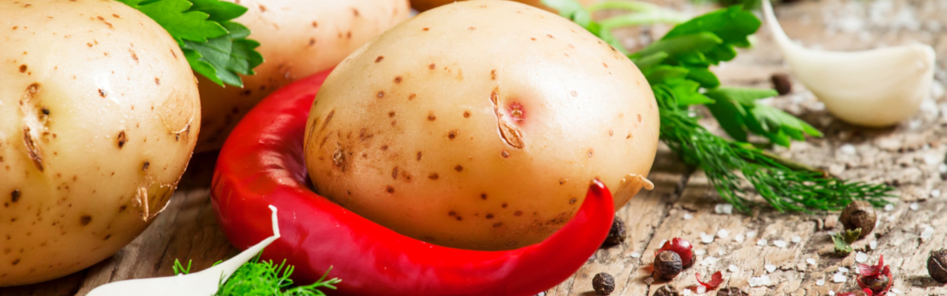 Frische Kartoffeln mit roter Chilischote, Kräutern und Gewürzen auf einem rustikalen Holztisch.